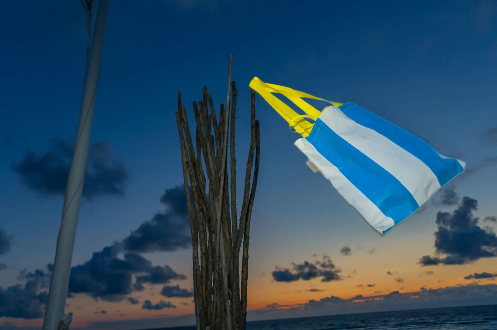 STURMflut Shopper Hellblau-Weiß aus Sylter Strandkorb-Bezug mit gelben Henkeln am Strand bei Sonnenuntergang — STURMFREI Upcycling
