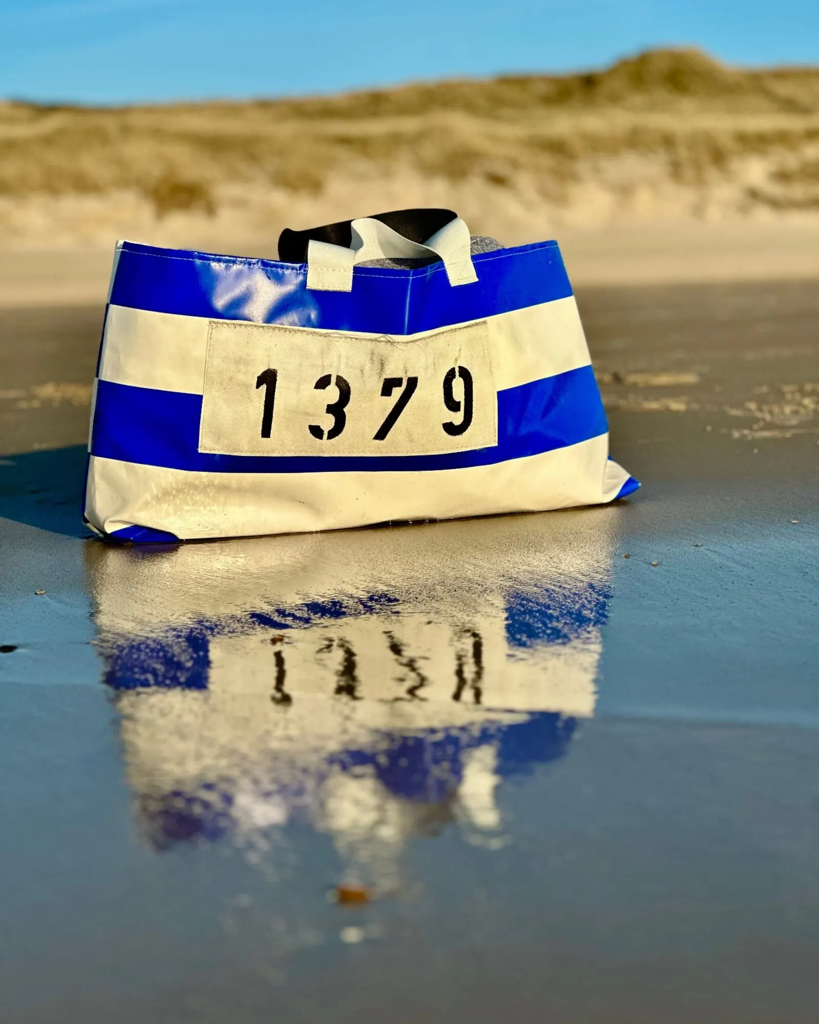 STURMflut XXL Strandtasche Königsblau-Weiß Nr. 1379 aus Sylter Strandkorb-Bezug am nassen Sandstrand vor Dünen — STURMFREI Unikat