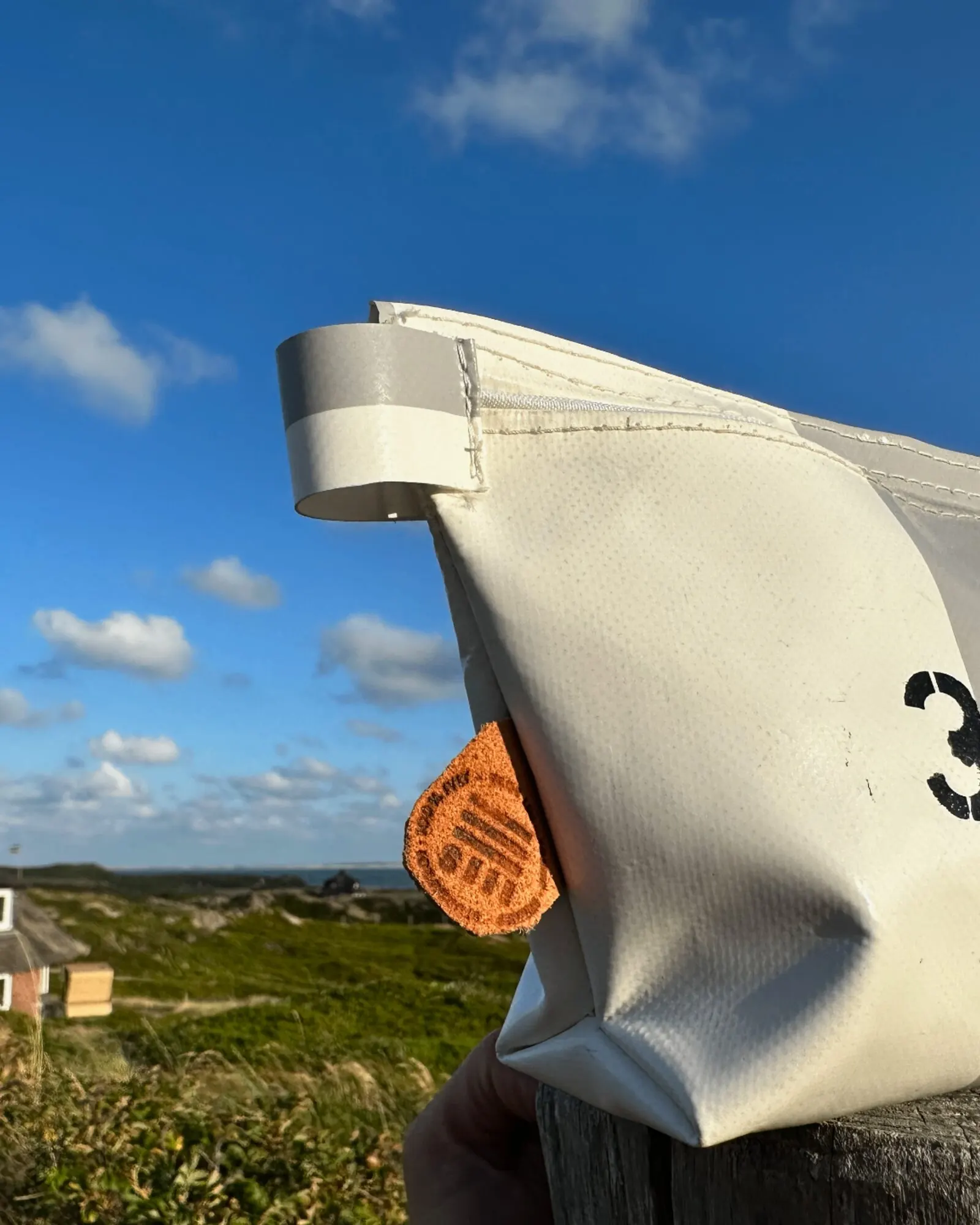 STURMleicht Kosmetiktasche klein Sand-Weiß Nr. 3.4.5 aus Sylter Strandkorb-Bezug vor Reetdachhaus und Dünen — STURMFREI Sylt